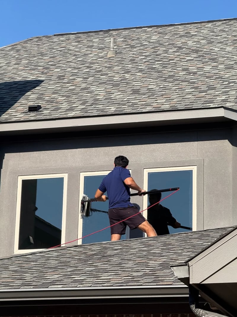 Technician using a water-fed brush on upper-story residential windows in North Dallas
