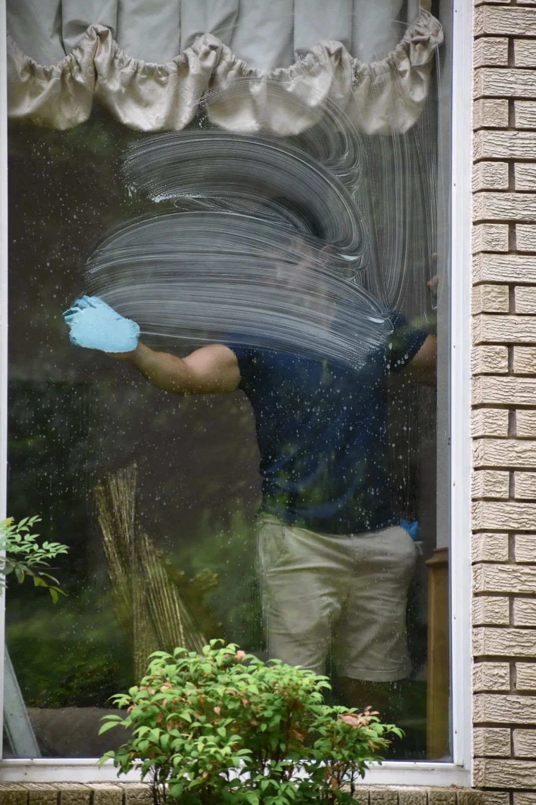 Topline Exteriors technician hand-detailing interior window glass at a Dallas luxury residence