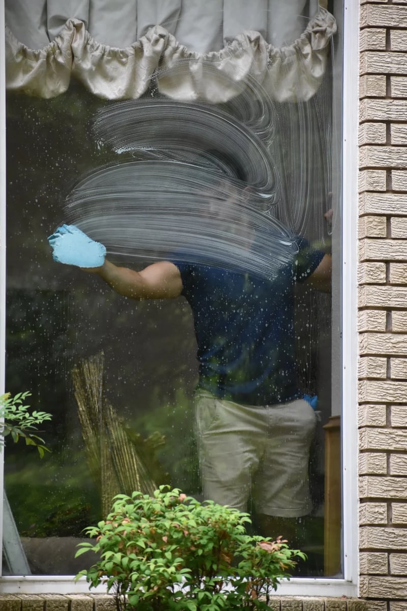 Topline Exteriors technician hand-detailing interior window glass at a Dallas luxury residence