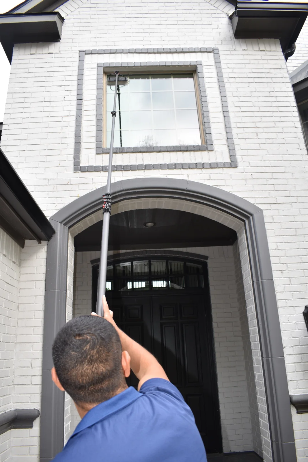 Topline Exteriors technician using a water-fed pole to clean residential windows