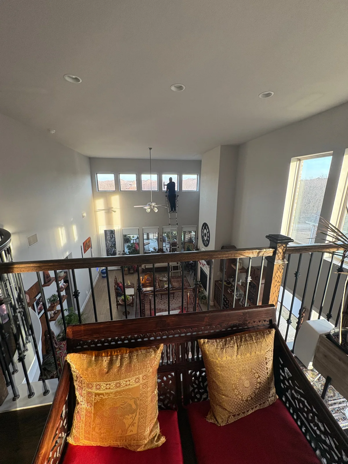 Technician detailing high interior windows from a ladder inside a two-story Dallas home