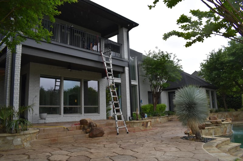 Professional multi-story window cleaning with ladder access at a poolside North Dallas residence