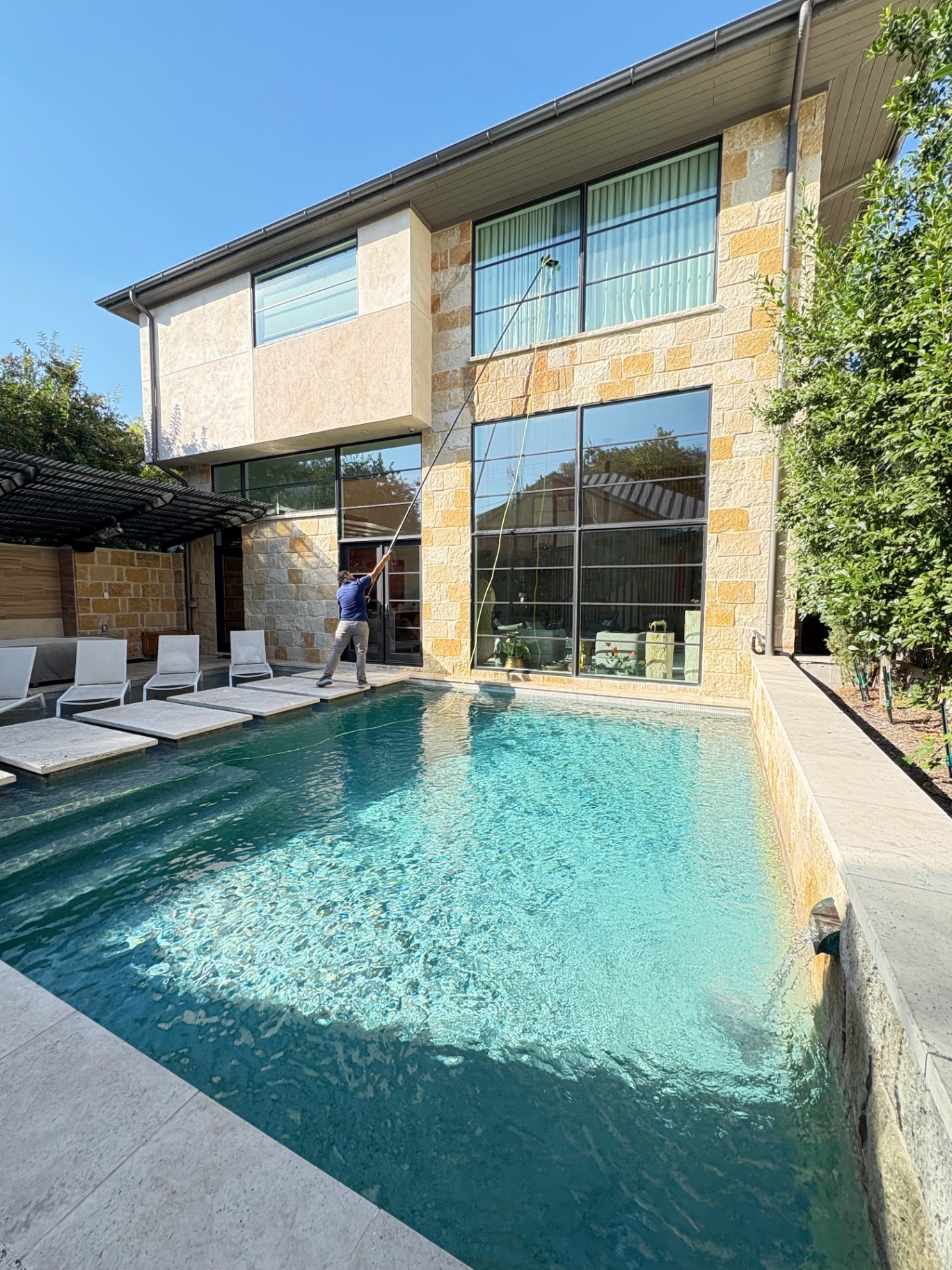 Pure-water pole window cleaning on a luxury modern home with poolside view